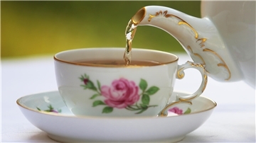 Tee wird aus einer Kanne in eine Tasse gegossen.