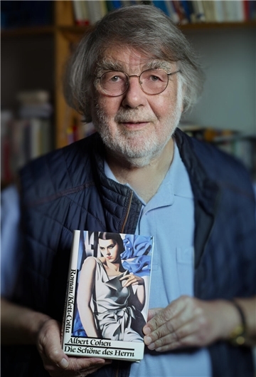 Ein Mann hält ein Buch mit der Aufschrift "Albert Cohen: Die Schöne des Herrn" und der Zeichnung einer Frau als Titelbild.