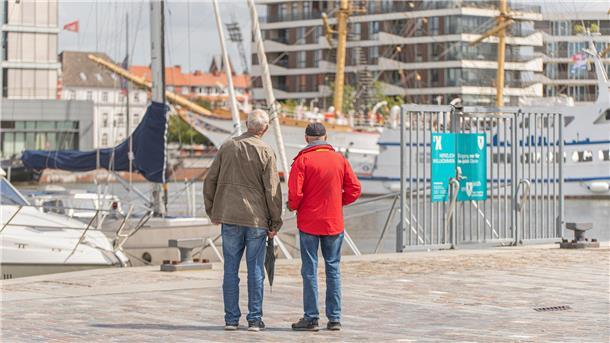 Zwei Männer blicken auf den neuen Hafen. Aus der Ferne wirkt der Hafen idyllisch, doch es gibt noch Baustellen.