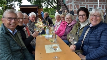 Eine Gruppe von acht Menschen sitzt an einer Biertischgarnitur und trinkt fröhlich Wein.