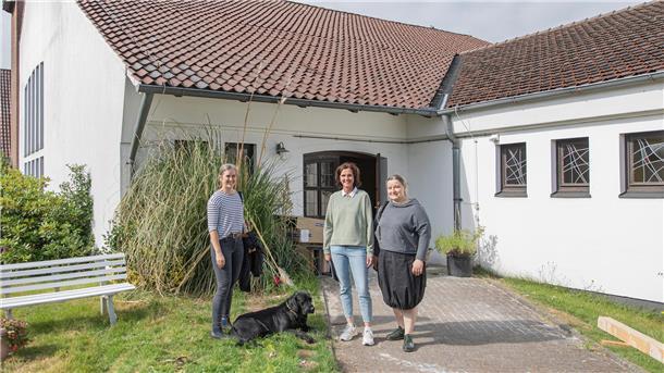 Drei Frauen und ein Hund vor einer Kirche im Umbau zur Tierarztpraxis.
