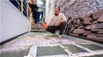 Ausstellung mit "doppeltem Boden": Dr. Philipp Grassel hebt ein Info-Puzzleteil hoch. Unter ihm ist die archäologische Grabungsstätte auf den Shetland-Inseln dargestellt. 
