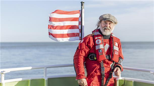 Autor Klaus-Peter Wolf auf einem Schiff. Im Hintergrund weht eine rot-weiß gestreifte Flagge.