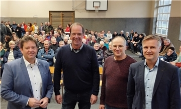 Vier Männer stehen vor einer größeren Menschengruppe