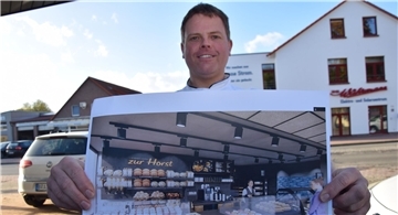 Ein Mann hält eine Skizze von einer zukünftigen Bäckereifiliale in die Kamera.
