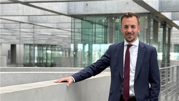 Ein Mann mit Anzug steht im Deutschen Bundestag und guckt in die Kamera.