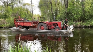 Bauer Sebastian Kilka aus dem Spreewald fährt den Miststreuer auf seinem Kahn über ein Fließ.