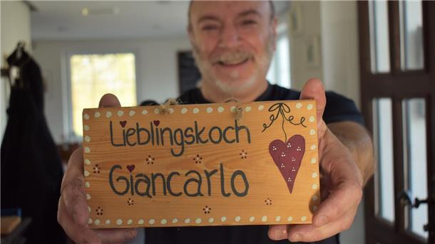 Ein Mann hält ein Schild in die Kamera. Darauf steht "Lieblingskoch Giancarlo" geschrieben.