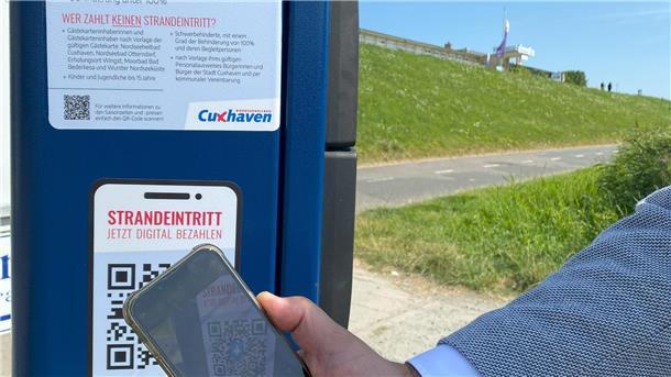 Eine Person scannt einen QR-Code am Strand.