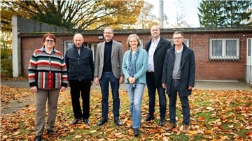 Zwei Frauen und vier Männer stehen nebeneinander auf einer Rasenfläche. Im Hintergrund ein Gebäude.