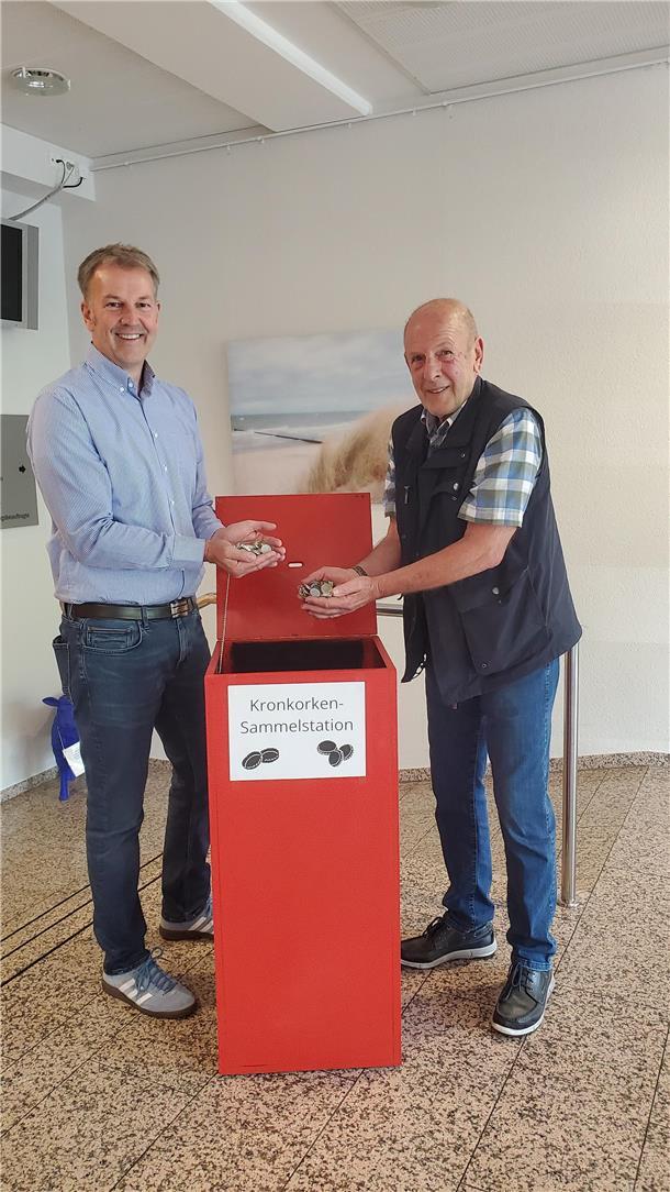 Beverstedts Gemeindebürgermeister Guido Dieckmann und Udo Kawaletz füllen die ersten Kronkorken in die neue Sammelstation im Beverstedter Rathaus.