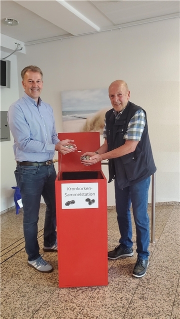 Beverstedts Gemeindebürgermeister Guido Dieckmann und Udo Kawaletz füllen die ersten Kronkorken in die neue Sammelstation im Beverstedter Rathaus.