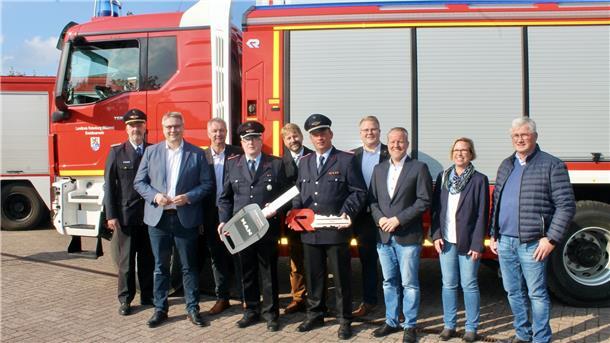 Landrat und Feuerwehrleute stehen vor einem Feuerwehrauto.
