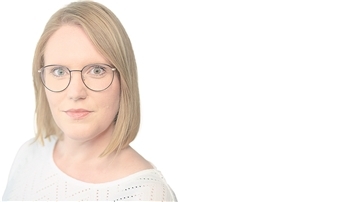 Eine blonde Frau mit schwarzer Brille schaut direkt in die Kamera.