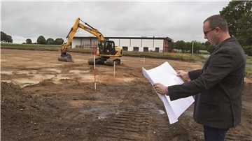 Ein Bagger steht auf einer Baustelle, daneben Markus Freiknecht.