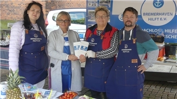 Drei Frauen und ein Mann stehen an einem Stand des Vereins "Bremerhaven hilft".