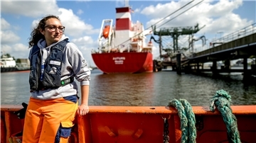 Frau steht vor Schiff.