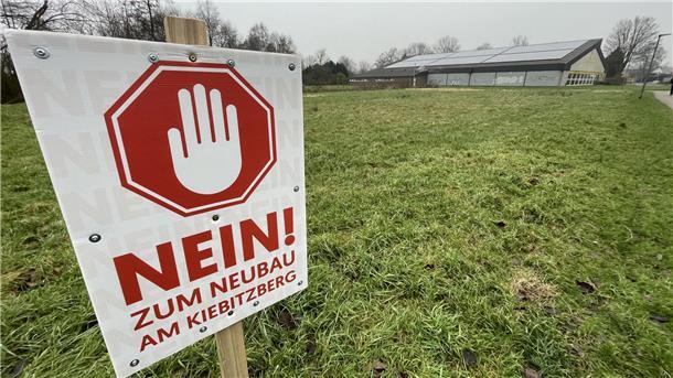 Schild mit der Aufschrift „Nein zum Neubau am Kiebitzberg" auf einer Rasenfläche.