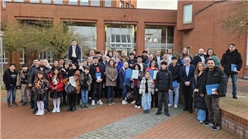 Eine große Gruppe von Menschen, darunter Erwachsene und Kinder, steht vor dem Kreishaus in Cuxhaven und posiert für ein Foto. Einige halten blaue Mappen in den Händen, während andere Deutschland-Fanschmuck tragen.