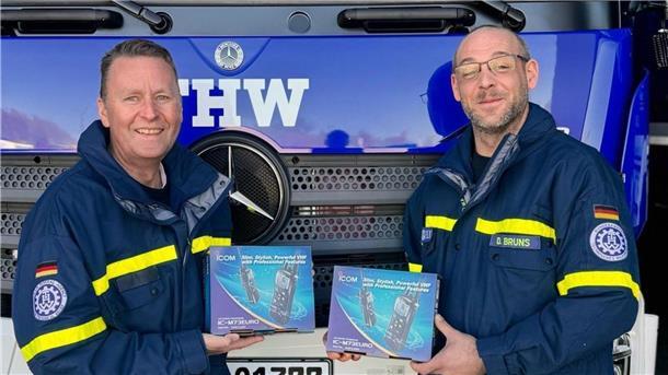 Zwei Männer stehen nebeneinander. In ihren Händen halten sie jeweils die Verpackung eines Seefunkgerätes.