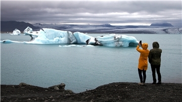 Zwei Touristen stehen in Island am Strand und fotografieren Gletscher