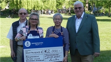 Vier Personen stehen im Freien auf einer Wiese, zwei davon halten einen großen symbolischen Spendenscheck über 2.000 Euro für den Verein "Bremerhaven hilft e.V." vom Förderverein Rotary Club Bremerhaven-Nordsee.