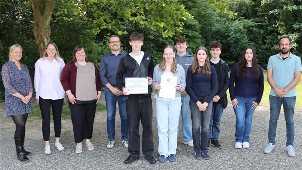 Schülerfirma erhält Landespreis für Nachhaltigkeit Gruppenfoto im Freien: Schüler:innen und Lehrkräfte der BBS Cuxhaven stehen gemeinsam, zwei halten Urkunden und eine Auszeichnung als „Nachhaltige Schülerfirma“.
