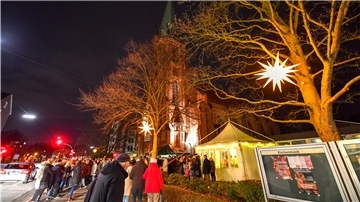 Lichterglanz auf Sparflamme Viele Menschen vor einer Kirche und Weihnachtsbeleuchtung an Bäumen.