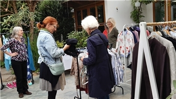 Mehrere Frauen stöbern an Kleiderständern im Freien nach Kleidung. Verschiedene Jacken, Blusen und Hemden hängen zum Tausch oder Kauf bereit.