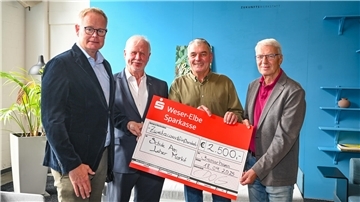 Vier Männer stehen nebeneinander und halten gemeinsam einen großen symbolischen Spendenscheck über 2.500 Euro.