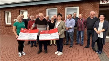 2.800 Euro für Wremens Jugend: Aale machen’s möglich Gruppenfoto von einer Spendenübergabe. Im Vordergrund halten drei Personen zwei symbolische Spendenschecks in die Höhe.