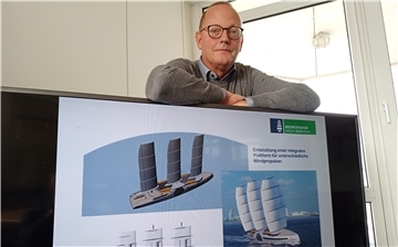 Mann hinter einem Fernseher, auf dem Schiffe zu sehen sind.