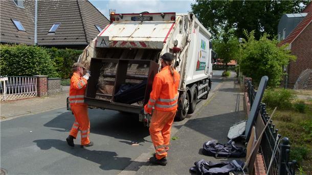 Zwei Männer in Arbeitskleidung tragen ein altes Regal in den Sperrmüllwagen.