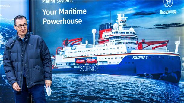 Ein Mann steht vor einem Plakat mit einem abgebildeten Schiff.