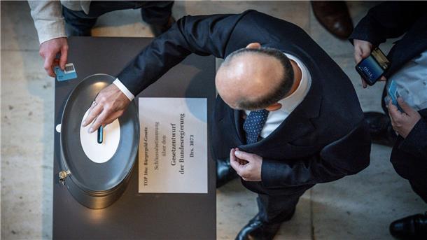 Bundeskanzler Olaf Scholz (SPD), wirft seine Stimmkarte zum Bürgergeld im Bundestag ein.
