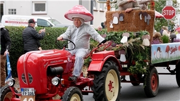 Eine Person fährt auf einem Traktor mit einem Festwagen dahinter.