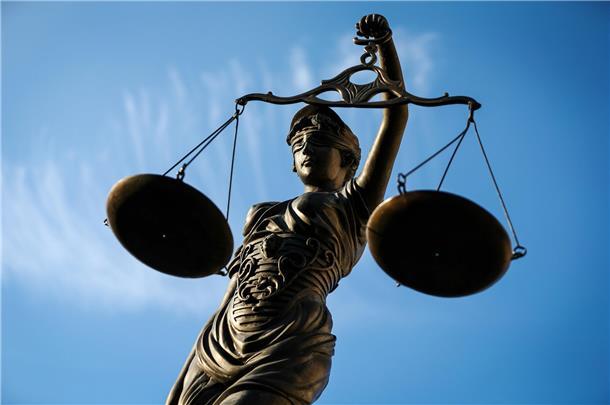Eine Figur des Jusizia hält eine Waage vor blauem Himmel. 