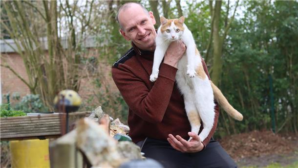 Christian Gerdon hält seinen Kater Tiger im Arm und blickt in die Kamera.