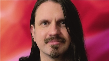 Mann mit langen Haaren und Bart vor einem roten Hintergund.