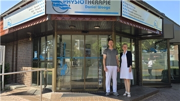 Christiane Thürlings, Vorstand der Raiffeisenbank, und Physiotherapeut Daniel Wooge stehen vor dem Praxisgebäude. 