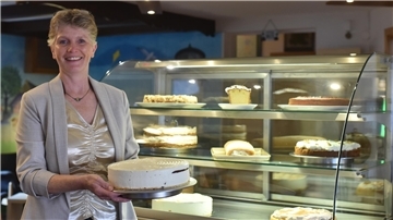 Eine Frau hält eine Torte in der Hand. Im Hintergrund sind weitere Torten zu sehen.
