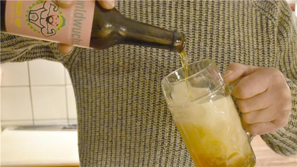 Eine Person schenkt ein Bier aus einer Flasche in ein Glas