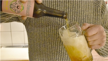 Eine Person schenkt ein Bier aus einer Flasche in ein Glas