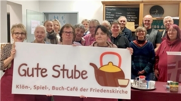Das Team der Guten Stube hält ein Schild hoch. 