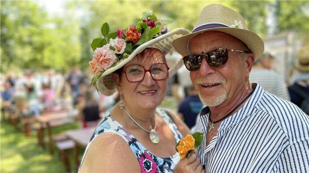 Ein Mann und eine Frau tragen in einem Park jeweils einen dekorativen Hut.