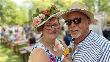 Ein Mann und eine Frau tragen in einem Park jeweils einen dekorativen Hut.