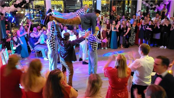 Bild von einer akrobatischen Vorführung einiger Männer und einem festlich gekleideten Publikum