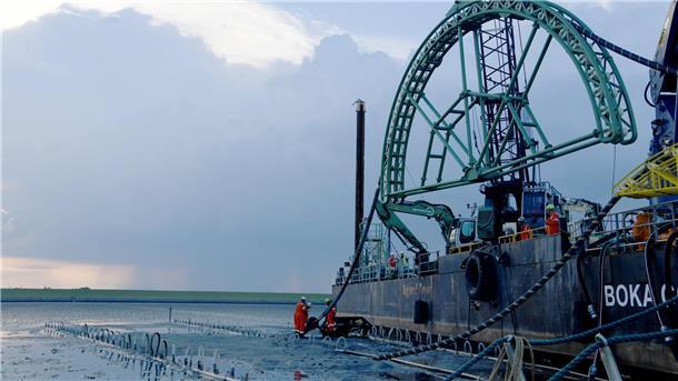 Ein Schiff mit einer Konstruktion zum Kabelverlegen steht im Watt