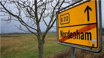 Rechts ein Ortsschild, links eine Weidefläche.