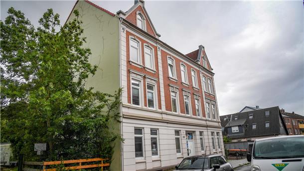 Mehrfamilienhaus mit rot-weißer Fassade in einer Wohnstraße.